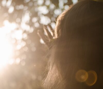 Sunlight glows warmly through a woman's hair beneath the trees, a picture of new life given