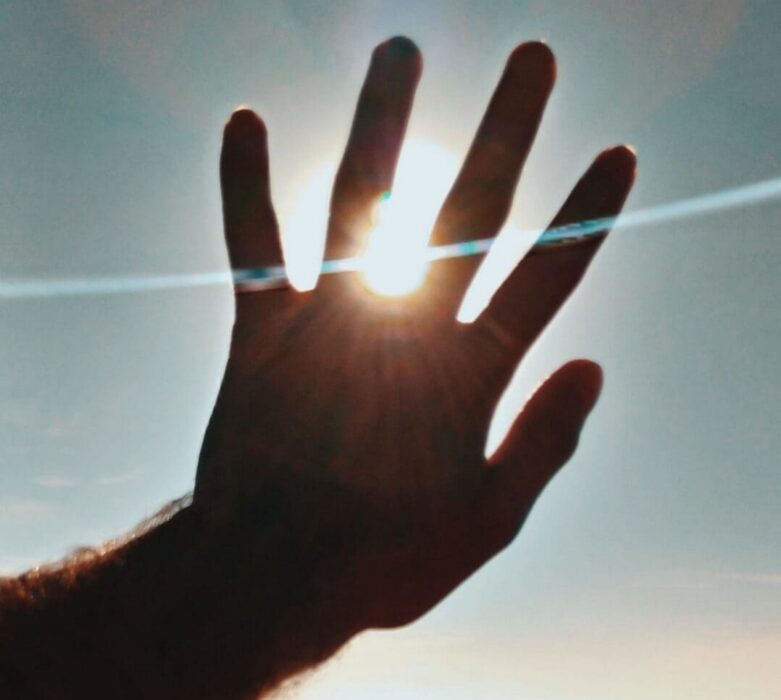 A hand reaches up toward the sun over open water, a picture of God working through weakness