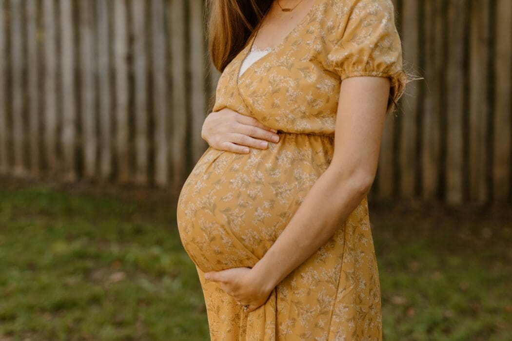 A pregnant woman in a yellow floral dress cradles her belly, echoing a long-awaited promise