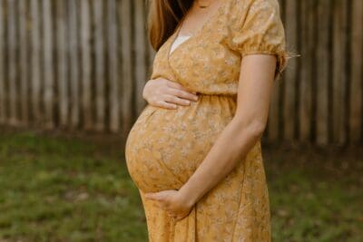 A pregnant woman in a yellow floral dress cradles her belly, echoing a long-awaited promise