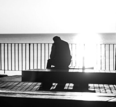 A lone silhouette sits facing the sea at sunset, a picture of sorrow held before God