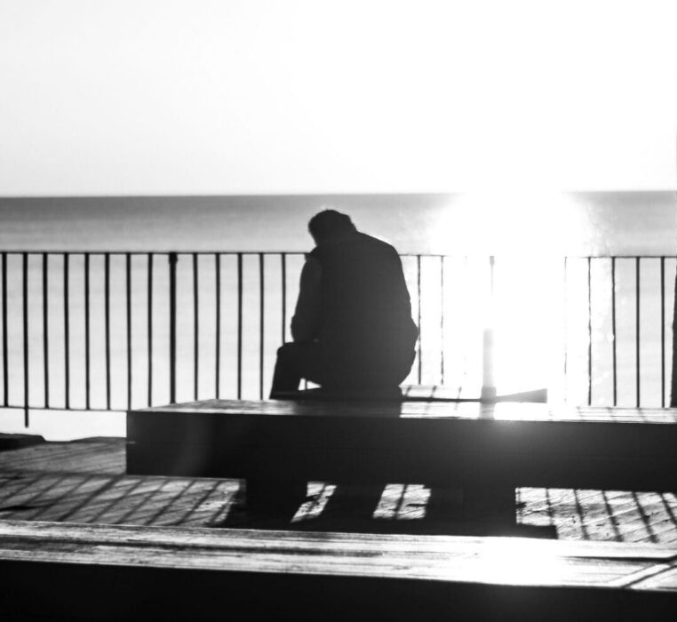 A lone silhouette sits facing the sea at sunset, a picture of sorrow held before God