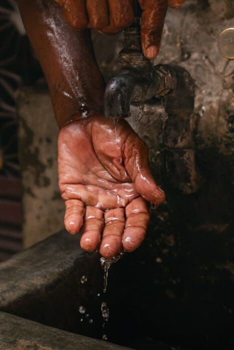 Water pours over cupped hands under an old tap, a picture of the cleansing sin demands
