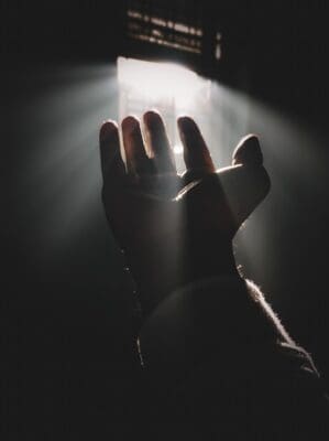 A hand reaches up into a shaft of light in a dark room, a picture of what God brings to light