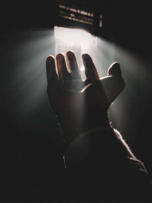 A hand reaches up into a shaft of light in a dark room, a picture of what God brings to light
