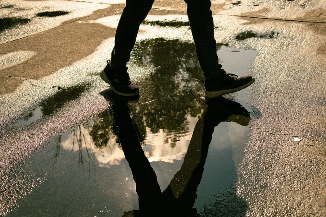 Feet step through a puddle reflecting the sky above, a picture of faith seeing beyond what's seen