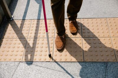 A cane taps ahead of careful footsteps on textured paving, a picture of trusting what can't be seen