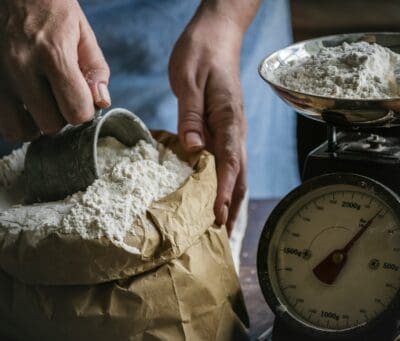 Flour is poured onto an old kitchen scale, echoing the flour sold cheap at Samaria's gate