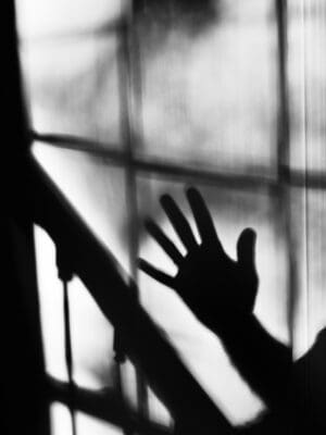 A hand's silhouette reaching toward light through a windowpane, echoing loving light over darkness.