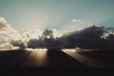 Dramatic storm clouds parting with sunbeams over a dark hillside, picturing judgment and hope together.