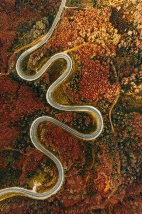 An aerial view of a winding road curving through a colorful autumn forest, picturing a journey of faith.