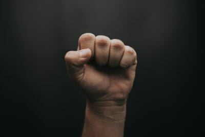 A clenched, raised fist against total darkness, picturing anger aimed at God over the world's evils.