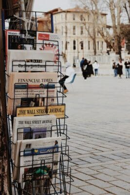 Outdoor newsstand racks of global papers and headlines, the kind of tragic news that can turn hearts to prayer.