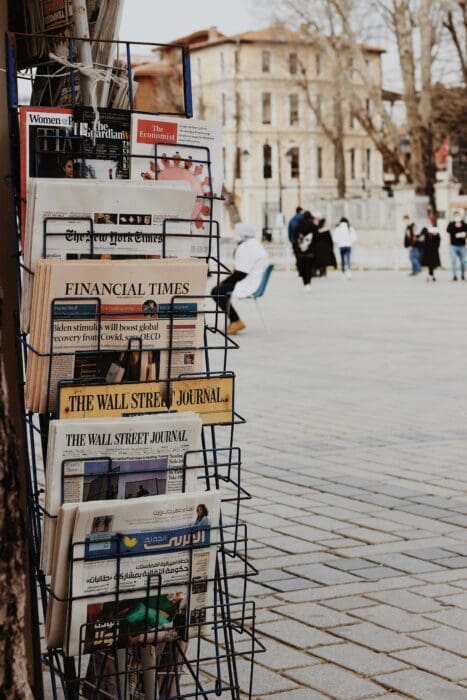 Outdoor newsstand racks of global papers and headlines, the kind of tragic news that can turn hearts to prayer.
