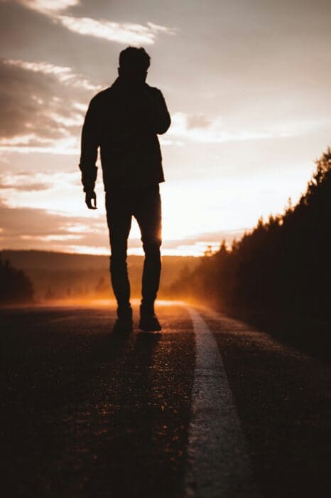 Silhouette of a man walking alone down a sunset road, like the rich young ruler leaving Jesus.