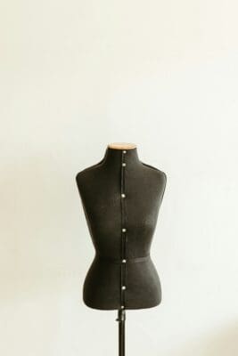 A faceless dress-form mannequin standing still against a plain wall, like 'Manny,' lifeless and unresponsive.